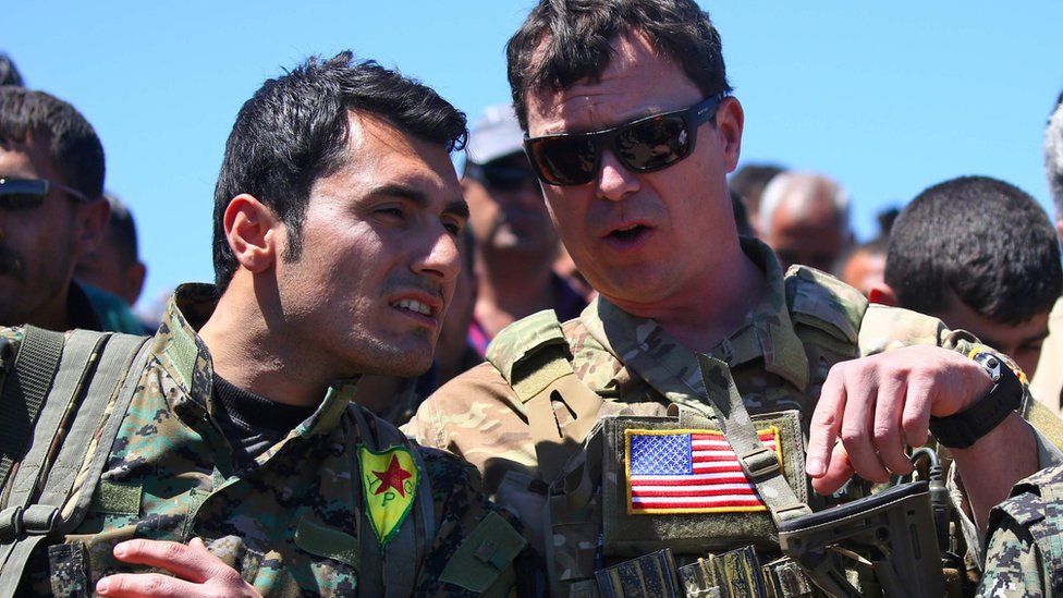 Kurdish YPG fighters speaks to a US military officer at the site of a Turkish air strike in northern Syria (25 April 2017)