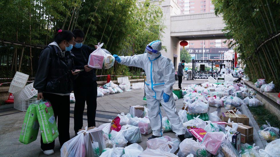 A volunteer wearing personal protective equipment (PPE) sorts bags of living necessities at the entrance of a locked-down residential community on November 7, 2020 in Zhengzhou