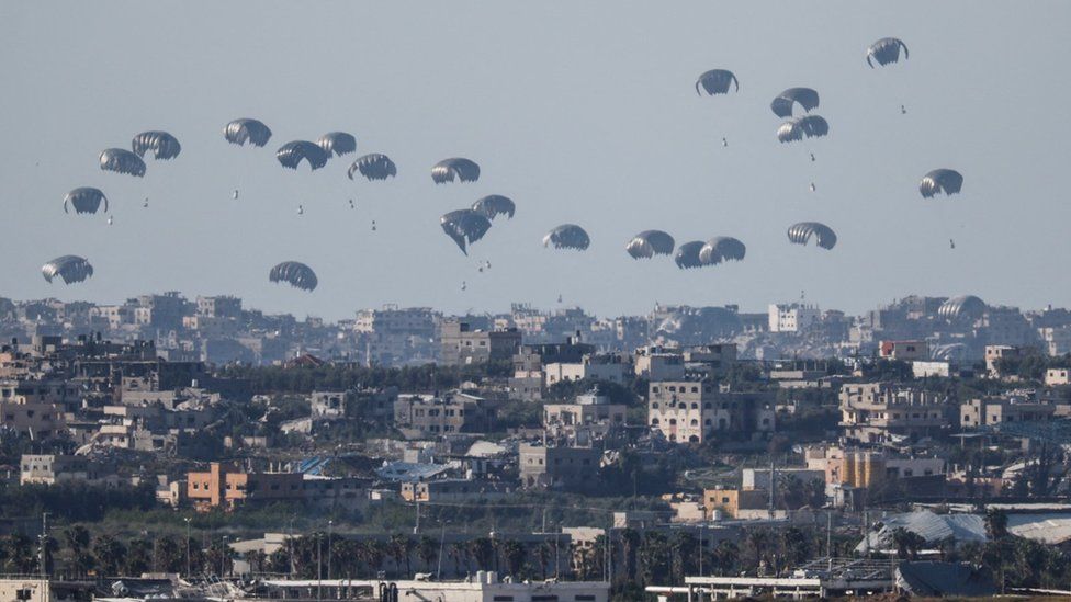 Humanitarian aid falls through the sky towards the Gaza Strip after being dropped from an aircraft