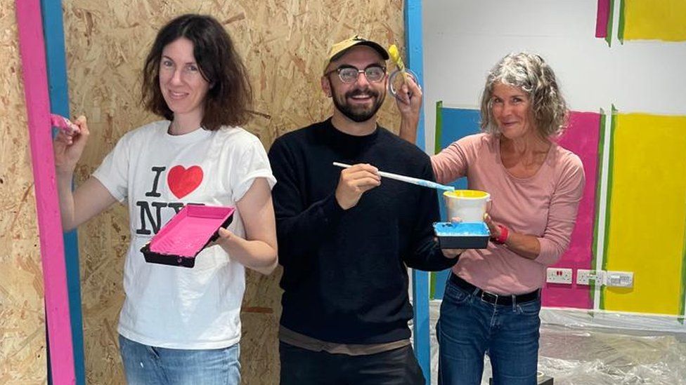 Talia Giles with two people painting inside the shop unit