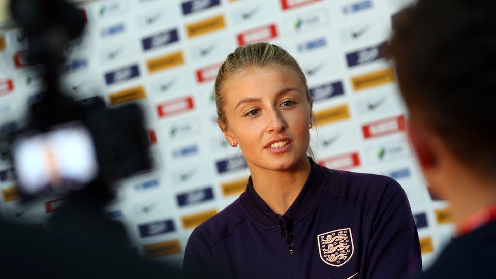 Leah Williamson being interviewed in front of a camera wearing an England sports jacket