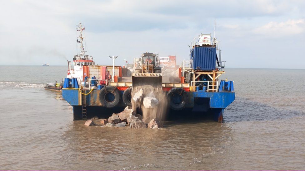 Large boulders being dropped into the sea by a blue barge