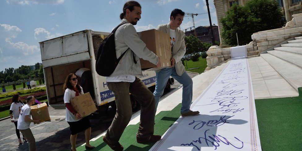 Volunteers unload dozens of boxes from a truck, crossing an oversized roll of giant signatures as they climb the senate steps in Bucharest