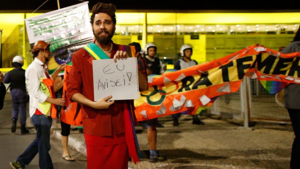 A protester dressed as impeached President Dilma Rousseff with a sign saying "I warned you!"