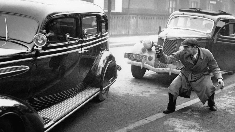 An armoured Chrysler Airflow car with ports for guns and 2 inch bullet proof glass, being tested by Scotland Yard officials in a mock battle with a 'gangster'. (P