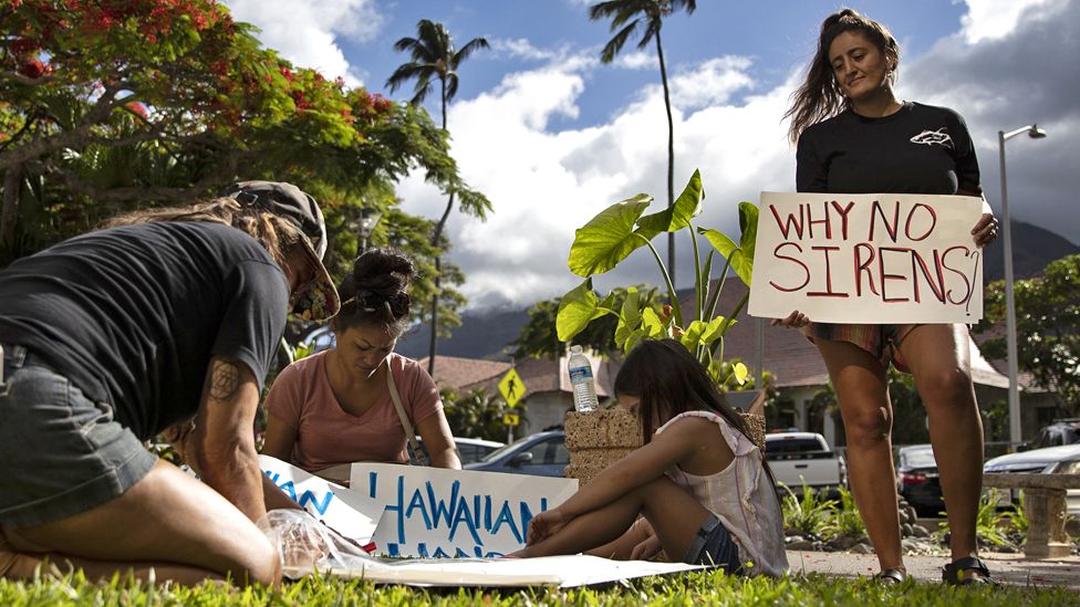Протестующий держит плакат с надписью «Почему нет сирен?» во время демонстрации людей перед зданием округа Мауи, где официальные лица провели пресс-конференцию, в Кахулуи, Гавайи, США, 14 августа 2023 г.