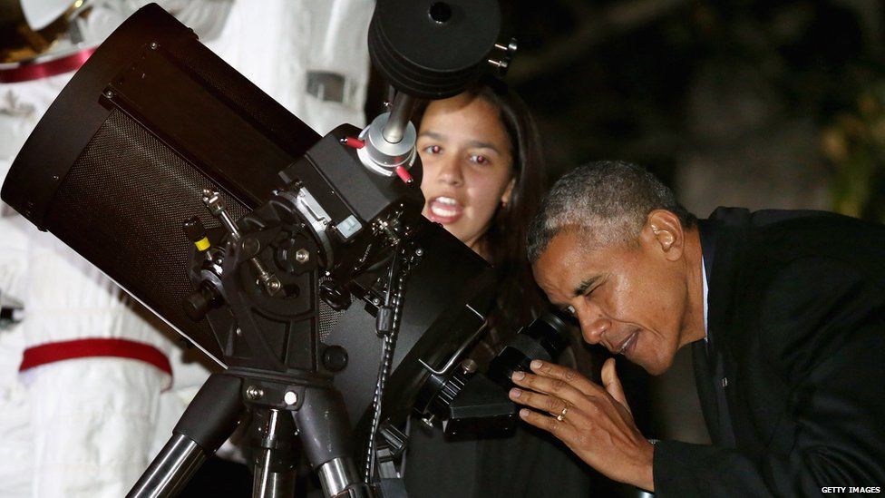 Barack Obama looks in a telescope