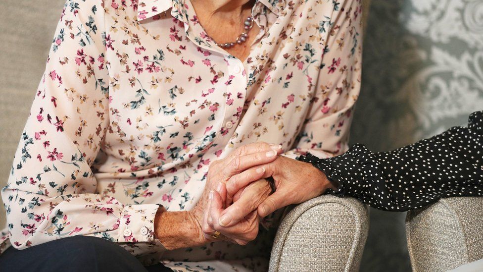 A care home resident holding hands with her daughter.