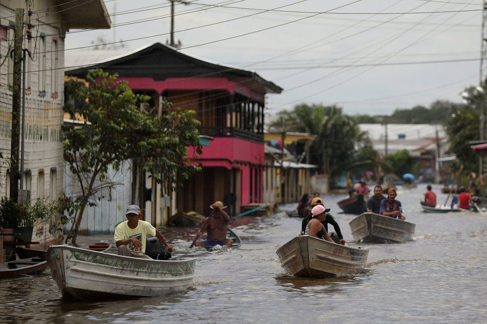 People pass on their boats through a street flooded by the rising Solimoes river