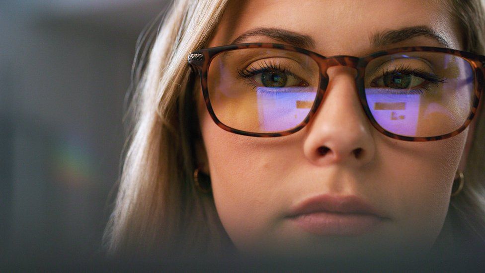 Крупным планом изображение женщины, смотрящей на компьютер с отражением экрана в очках