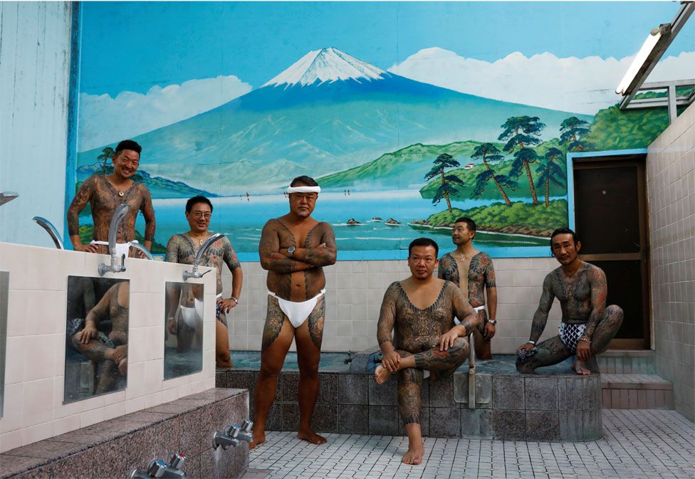 A group of men with tattoos pose in a public bath