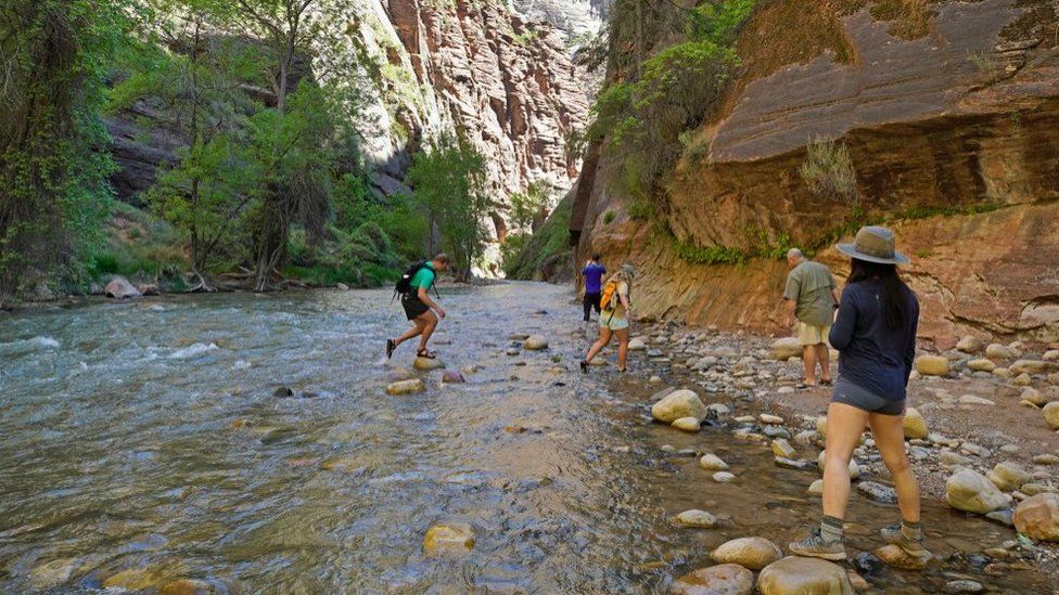 Hikers take pictures at the entrance of the famous Narrows hike in Zion National Park, Utah