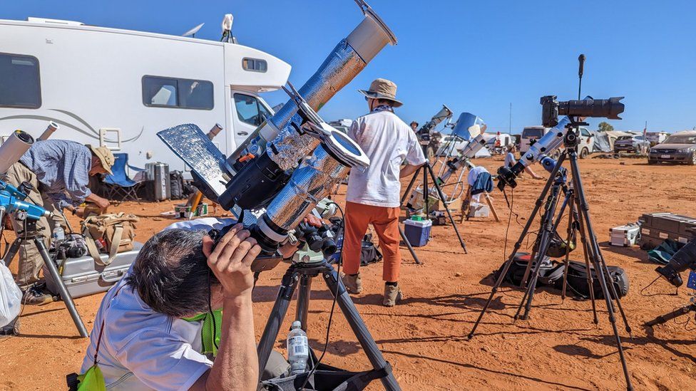 人们使用望远镜和照相机观看日食