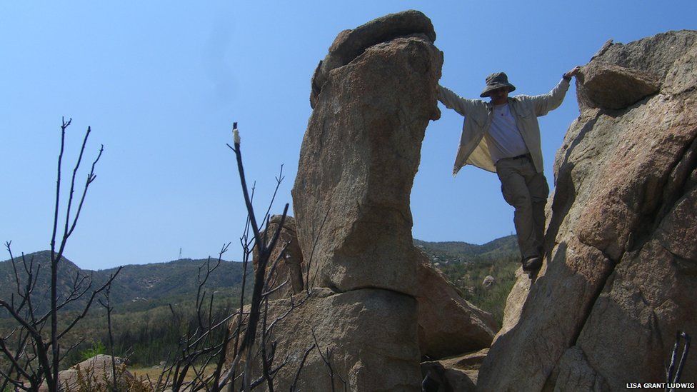 one of the researchers straddles a balancing rock in California