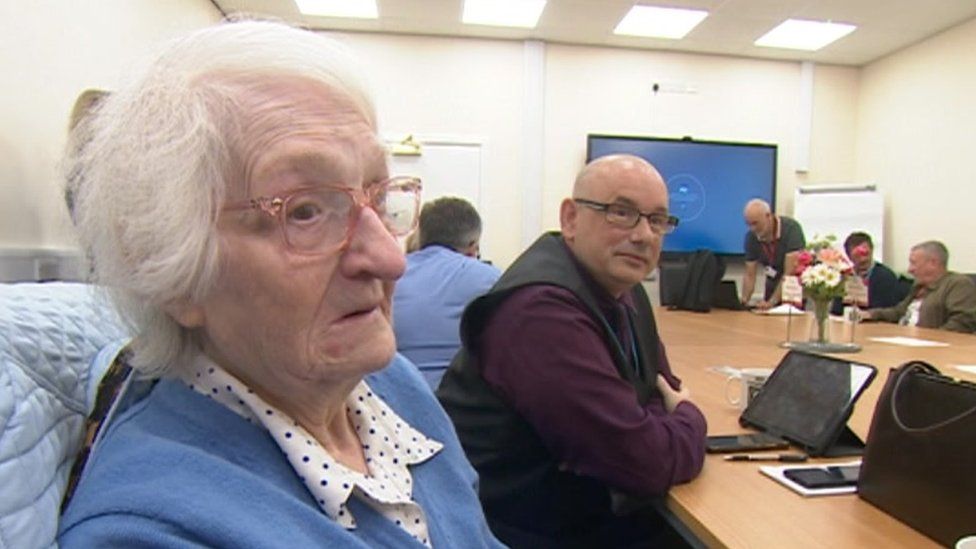 An elderly woman in a blue jumper being interviewed