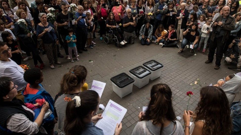 People stand around ballot boxes during a tribute outside a school which acted as polling station in the referendum and was subsequently raided, during a regional general strike to protest against the violence that marred Sunday's referendum vote (03 October 2017)