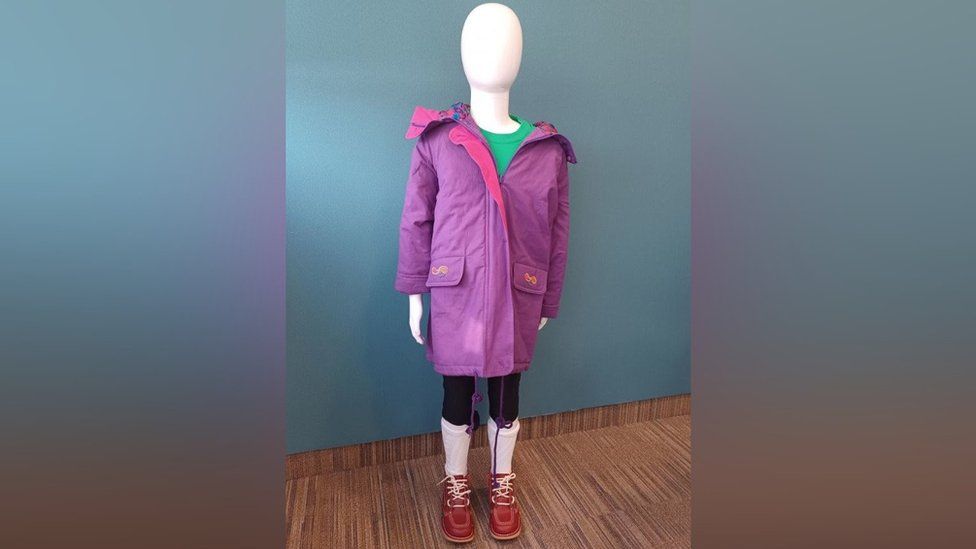 A mannequin with a purple coat, green shirt, black leggings, white socks and red shoes