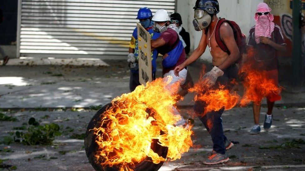 Opposition demonstrators use a tire on fire to block a street in Caracas. Photo: 26 July 2017