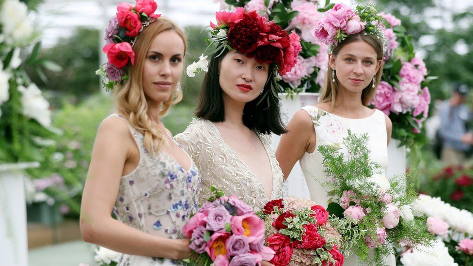 Three women with flower bouquets and floral head decorations