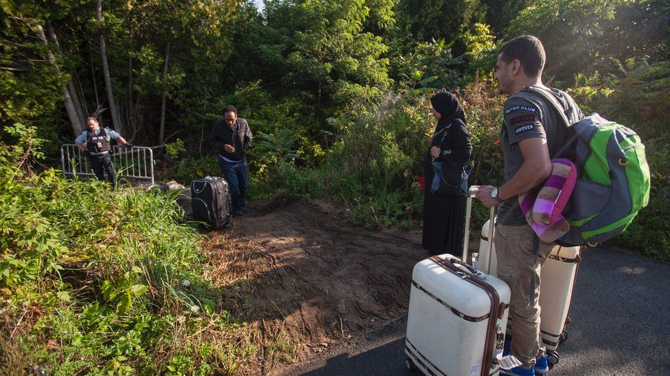 RCMP officers speaks with migrants as they prepare to cross the US/Canada border illegally near Hemmingford, Quebec, August 20, 2017.