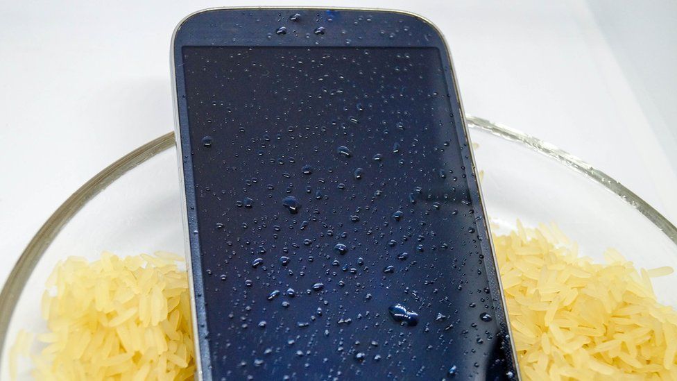 A phone in a bowl of dry rice - stock image