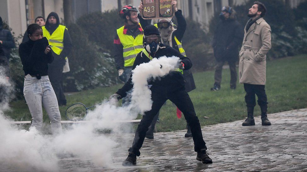 A protester - wearing a soon-to-be-banned face covering - throws back a police gas canister on 19 January