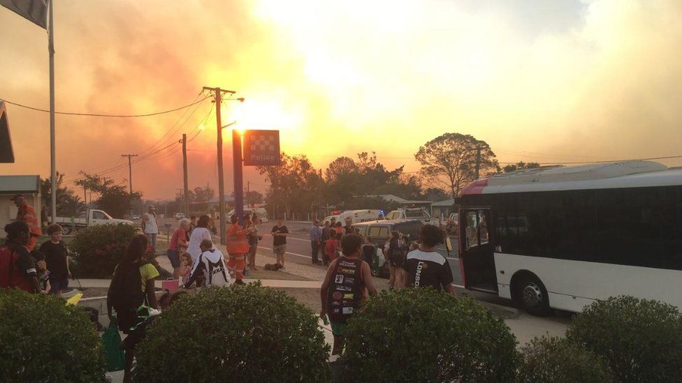 Emergency workers and locals outside the Gracemere Police Station organise to leave the town as the fire taints the sky