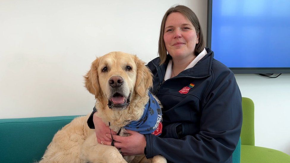 An adorable golden retriever sits on the lap of a woman in a Salvation Army uniform