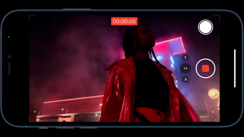 An iPhone is shown shooting a challenging scene at night with backlit neon lights