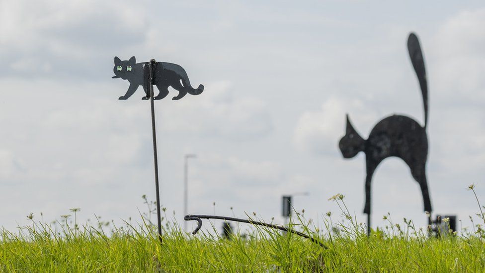 A small black cat sculpture by a larder black cat sculpture