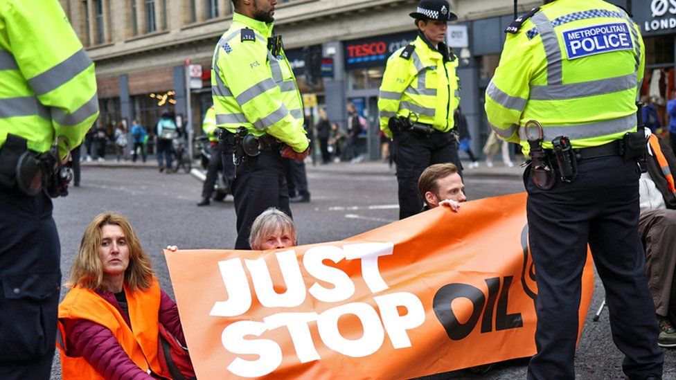 Police officers gather around activists blocking a road during a Just Stop Oil protest in London on 30 October 2022