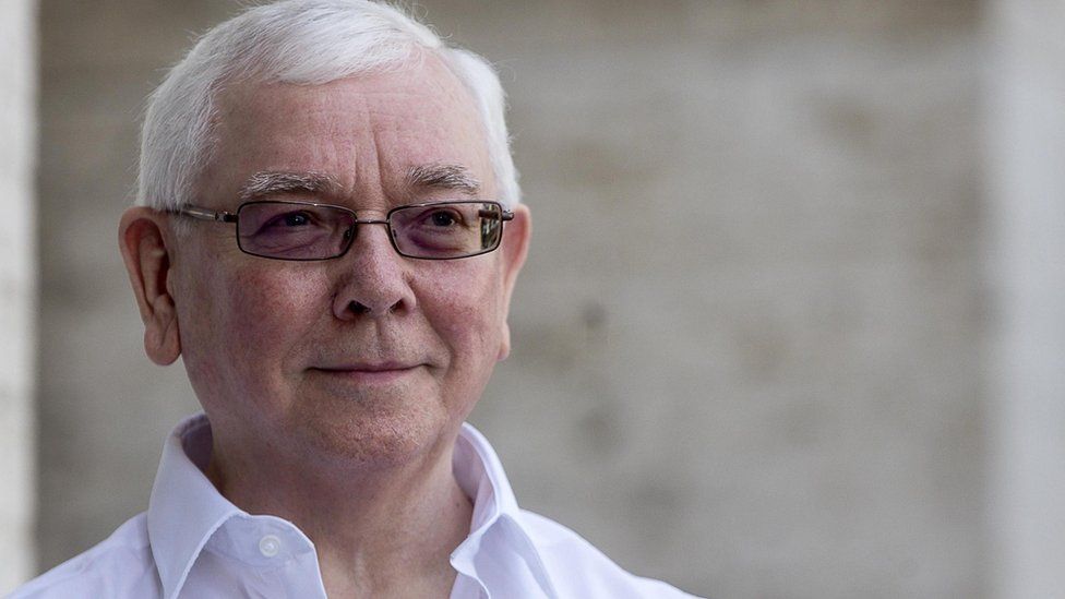 Terence Davies, wearing a white shirt and glasses, looking off camera