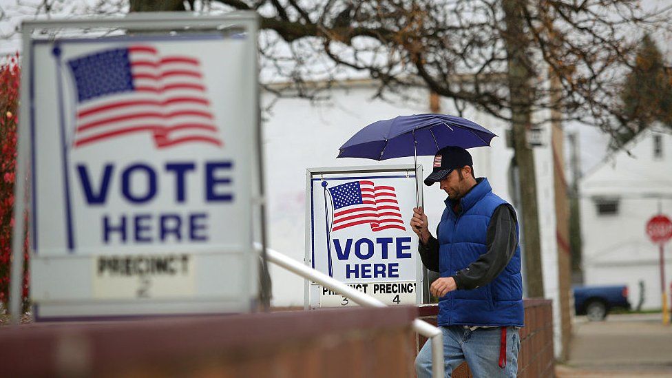 A man with umbrella walks past voting signs displayed outside a polling station during the mid-term elections