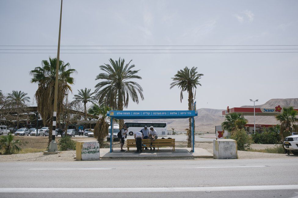 Orthodox Jewish boys sit in the shade at a bus stop near the Palestinian town of Jericho in West Bank