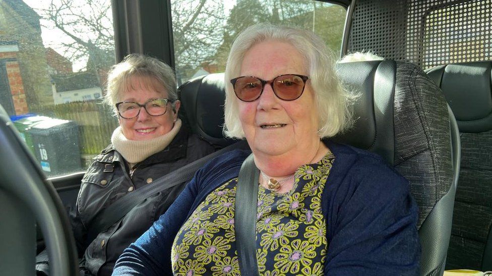 Two elderly women wearing glasses sit on a bus