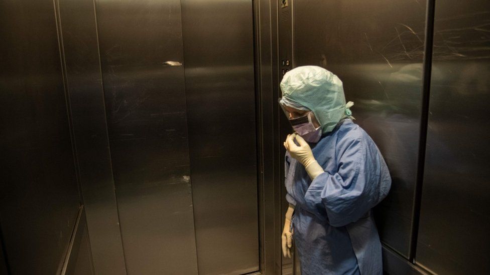 An nurse wearing protective clothing stands in a lift in Turin