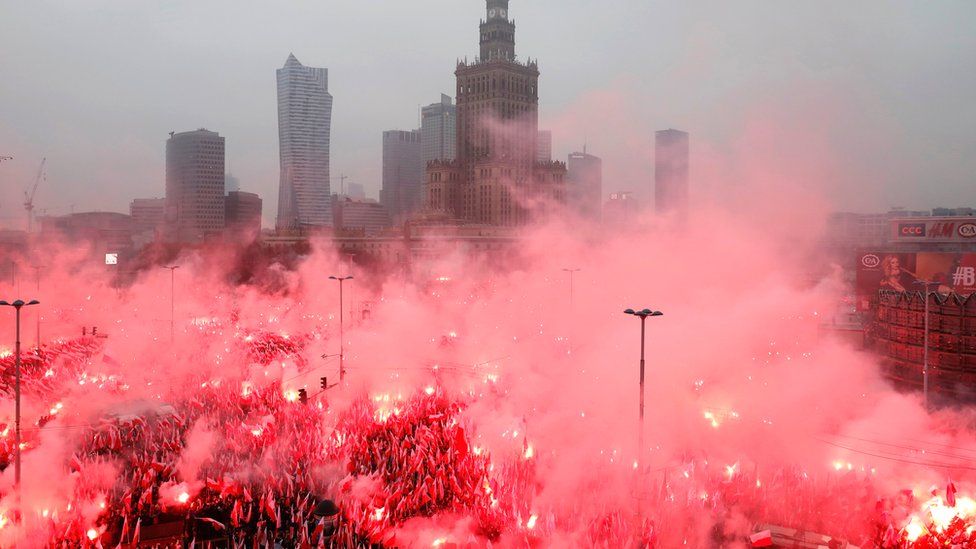 People carry Polish flags and flares as they sing Polish national anthem during a march marking the 100th anniversary of Polish independence in Warsaw, 11 November 2018