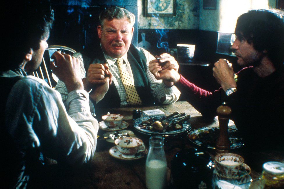 Uncle Monty (Richard Griffiths) sits at the cottage table with Withnail and Marwood