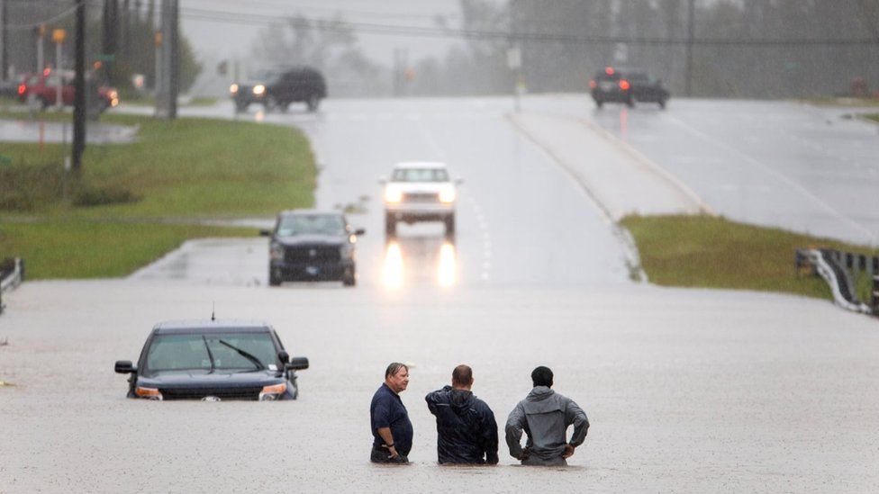 Men stand waist-deep in water, as a car is submerged heavily in Holly Ridge, North Carolina