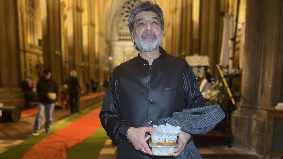 Arif Khan pictured standing in the cathedral holding a box of food
