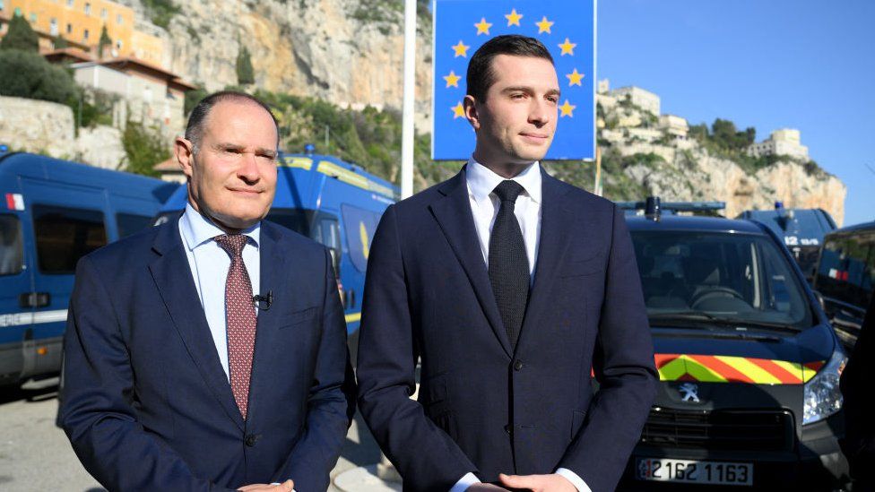 French far-right Rassemblement National (RN) party President Jordan Bardella (R) and RN party member and former head of the EU's border agency Frontex Fabrice Leggeri (L) look on, with a sign reading "Italy" and French gendarmerie vehicles in the background, during a visit at a border crossing between France and Italy in Menton, southeastern France, on February 19, 2024