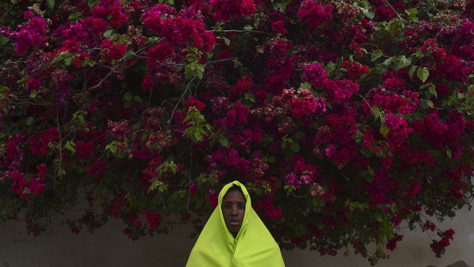 A woman with a yellow headscarf posing under a tree with flowers.