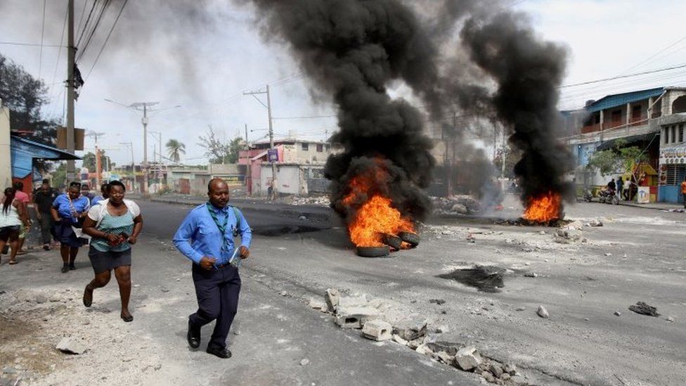 People walk past a burning street barricade during a demonstration against fuel shortages, in Port-au-Prince, Haiti October 23, 2021.