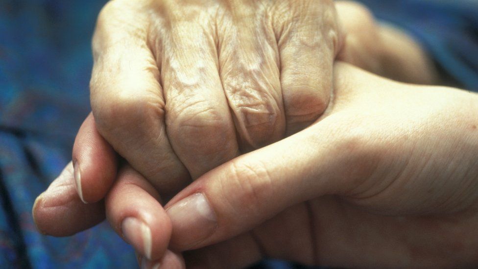 Close-up of an elderly person holding the hands of a younger person
