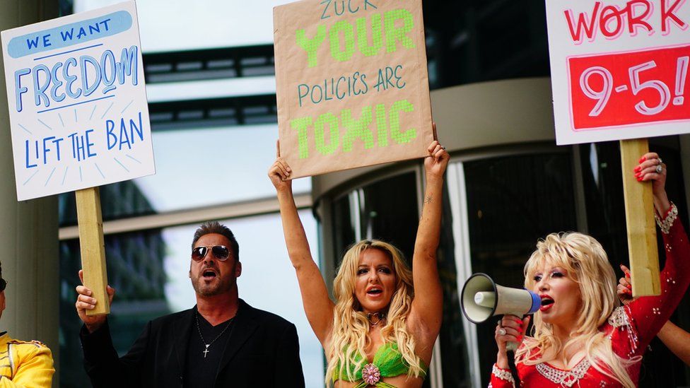 Impersonators staging a protest with placards outside Meta HQ - George Michael ("We want Freedom - lift the ban"), Britney Spears ("Zuck - your policies are toxic") and Dolly Parton, holding a megaphone ("Let's work 9-5")