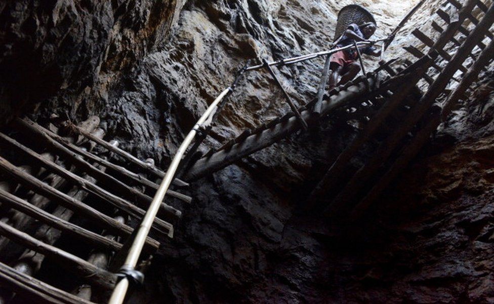 Шахтер несет тяжелый груз влажного угля в корзине на высоте сотни футов на деревянных планках в глубокой угольной шахте в Мегхалае.