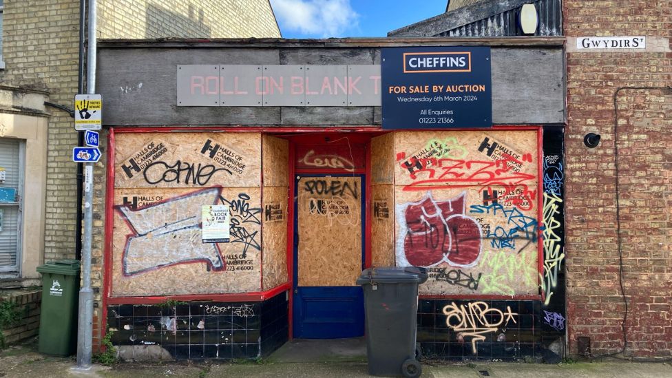 The closed shop with boarded-up windows, graffiti and a for-sale sign