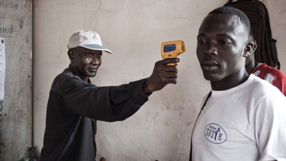 A health worker monitors the temperature of a traveller from the DR Congo
