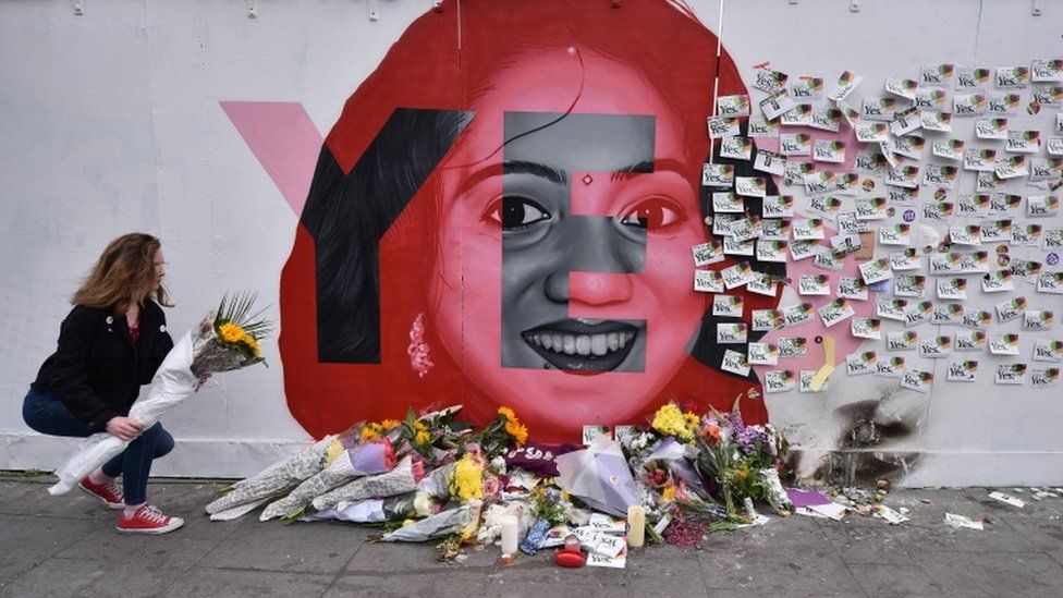 A young woman leaves flowers at the Savita Halappanavar mural in Dublin