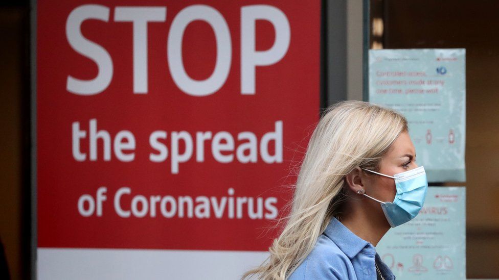 A woman walking past a coronavirus warning sign in Glasgow